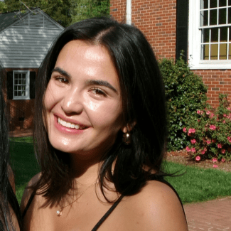 a young woman with curly dark hair smiling in front of a brick building