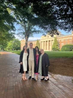 a group of four young people in graduation robes smile in front of a large academic building with a rotunda and columns on a sunny evening