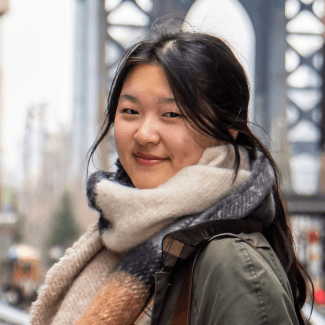 a young woman wearing a scarf and jacket in front of a bridge on a cloudy day