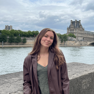 a young woman standing in front of the Seine River on a cloudy day