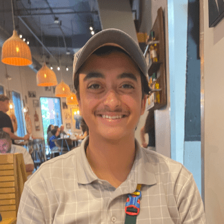 a young man wearing a hat and collared shirt sitting in a restaurant