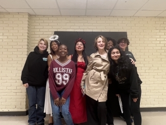 Group of high school students huddle in front of a white brick wall