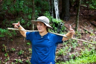 a young woman smiles while holding a hiking stick in the woods