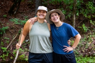 two young women smile together in the woods hiking
