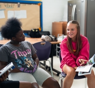 two young women read together and smile