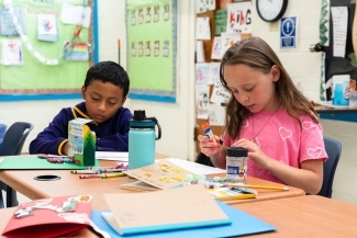 two young people work on crafts at a table