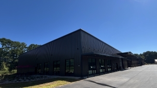 A warehouse-shaped metal building with rows of vertical windows and concrete around the perimeter