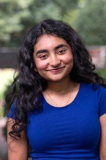 Female student with blue shirt and dark, long hair smiles softly