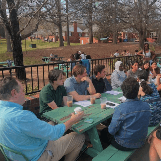 a group of students meet with a professor at a picnic bench