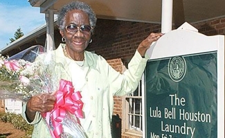 An older black woman holding a bouquet of flowers with a pink ribbon