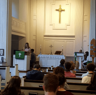 Blonde student stands behind a pulpit in a Catholic church