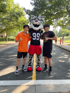 two young men smile with a Wildcat mascot in running gear