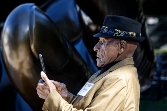 Sammie Ross, wearing a hat and light brown jacket, takes a photo of the sculpture