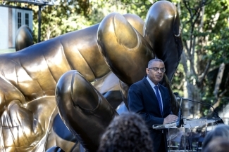 Anthony Foxx addresses the crowd at the podium in front of the hands sculpture