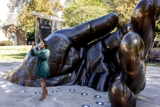 Woman in green dress takes selfie in front of With These Hands sculpture