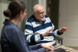 Veteran Sam Maloney ’48 speaks to a female journalist in the foreground, gesturing while wearing a striped shirt