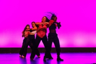 a group of your women dance onstage in front of a magenta backdrop