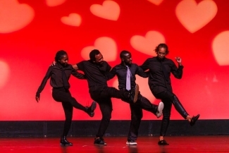 a group of four students do kicks during a dance onstage