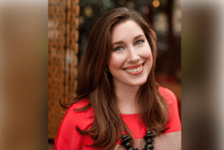 a young woman wearing a bright coral top with brown hair smiling