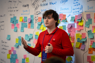 Male student with brown hair and red Davidson branded pullover presents in front of a wall of sticky notes