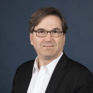 a middle aged white man wearing a white shirt, black jacket and glasses