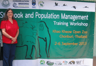 A woman in a red shirt stands next to a large green banner for the "Studbook and Population Management Training Workshop" at Khao Kheow Open Zoo, Thailand.