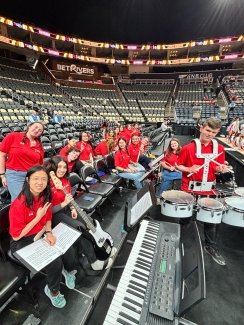 Alt Text Generator Custom Gem Alt Text Generator said A group of pep band members in red shirts pose with their instruments, including a keyboard, bass guitar, and quads, in the stands of a large, mostly empty arena during an Atlantic 10 tournament event.