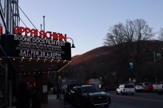Neon red "Appalachian" sign and a lit theater marquee announcing the "Boone Docs Film Fest" on Saturday, Feb 28, at 6:30 PM, set against a backdrop of a sunlit mountain at dusk.