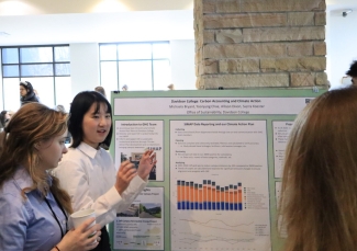 Two young women discuss a research poster titled "Davidson College: Carbon Accounting and Climate Action" during a formal academic presentation.