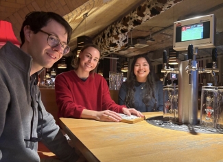 Three friends smile at a pub table equipped with a self-service beer tap and a digital touchscreen display.