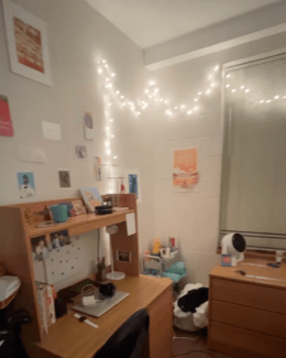 A wooden student desk with a hutch sits against a white wall decorated with string lights, small photos, and an orange sunset poster.
