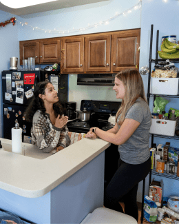 two young women stand in a kitchen having a conversation
