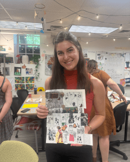 A smiling student holds up a handmade collage featuring black-and-white illustrations and text snippets in a bright, decorated art studio.