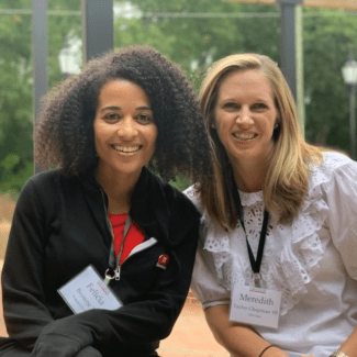Two women, Felicia Browne and Meredith Taylor Chapman ’05, smile together while wearing Davidson College name tags at an outdoor event.