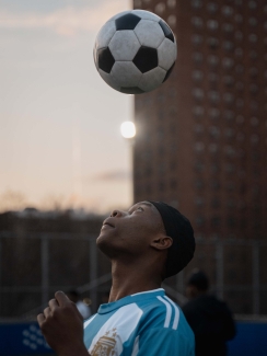 A young man in a blue jersey looks up at a soccer ball suspended in air