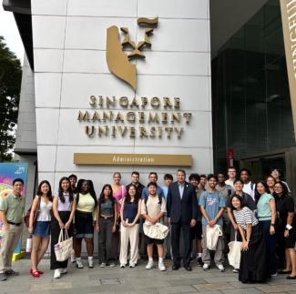 A large group of diverse students and faculty pose for a group photo in front of the Singapore Management University administration building entrance