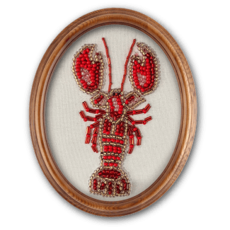 An oval-framed embroidered piece featuring a textured red and gold beaded lobster on a white fabric background.