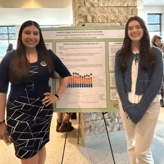 Two students stand on either side of a large research poster titled "Davidson College: Carbon Accounting and Climate Action" during an indoor academic presentation.