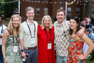 Five alumni or guests pose together smiling for a group picture wearing name lanyards (marked "Reunion '26").