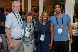Four attendees pose closely together smiling, each wearing lanyard name tags reading "Reunion '26".
