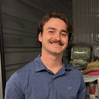 A smiling young man with brown hair and a mustache wearing a blue polo shirt