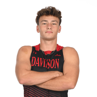 A young man with brown hair poses with crossed arms, wearing a black and red Davidson athletic jersey against a solid white background.