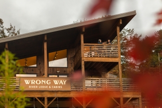 A wooden two-story building featuring a large sign reading "Wrong Way River Lodge & Cabins" framed by autumn leaves.