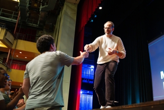 A man onstage hands something to an audience participant