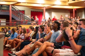 A row of students smiling, clapping, laughing and cheering in a red auditorium
