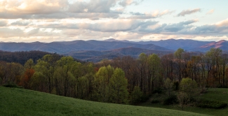 Panoramic view of lush green trees and rolling blue mountain ridges under a cloudy twilight sky.