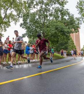 Two male runners stride past spectators down a wet asphalt road during a race.