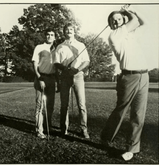 A black-and-white photograph showing a golfer mid-swing on a golf course while two other men stand behind him watching his shot.