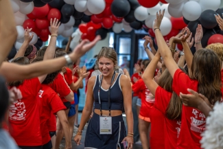A female student smiles and walks through the balloon tunnel, shoulders scrunched