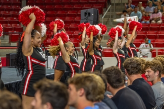 Cheerleaders with black and red uniforms hold red pom-poms overhead